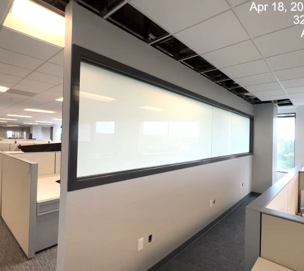 Office hallway with cubicles and a large frosted glass partition under fluorescent ceiling lights