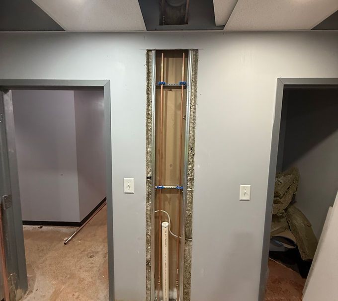 Partially stripped wall with exposed wiring between two open doorways in a room under renovation
