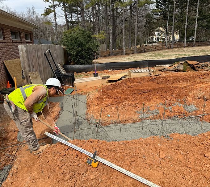 Worker in a hard hat smoothing fresh concrete at a construction site with dirt and wooden forms