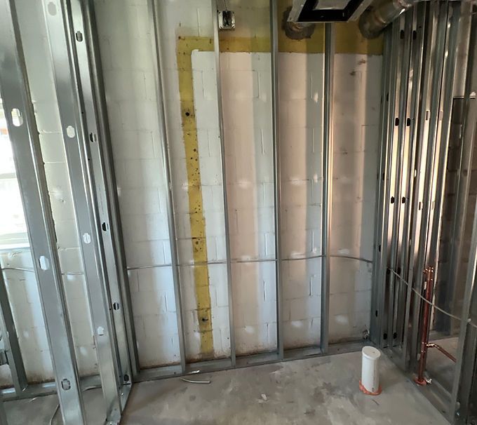 Partially framed interior wall with drywall panels, exposed studs, and electrical conduit in a construction site