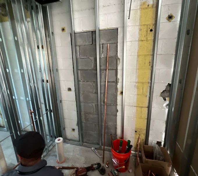 Partially finished room with exposed metal framing, cinder blocks, tools, and a worker in the foreground