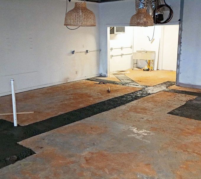 Empty room with worn brown floor, dark floor strips, and a bright doorway to a smaller kitchen area.