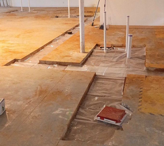 Partially renovated floor with exposed pipes and covered sections in an unfinished room