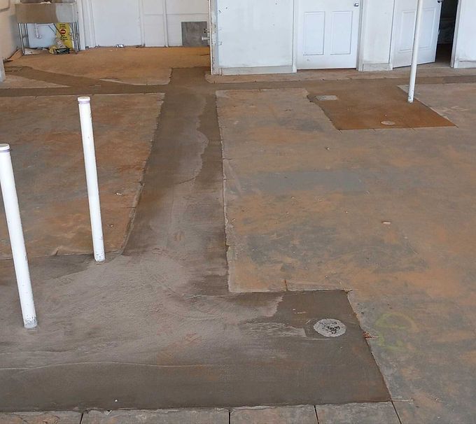 Unfinished concrete floor with patchwork seams and white pipes in an empty interior room