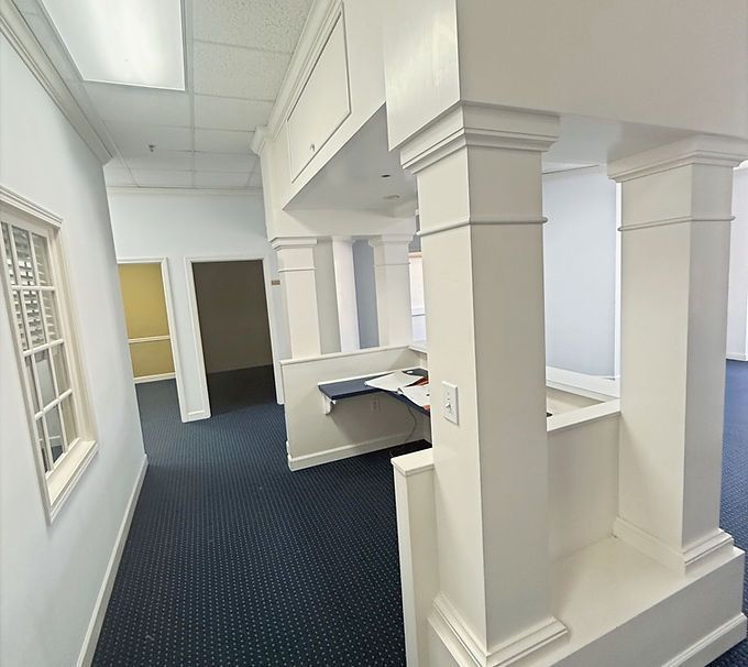 Empty office hallway with white columns, blue carpet, and a windowed wall