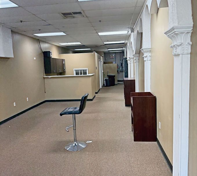 Empty beige room with carpet, bar stool, and a service counter in the back