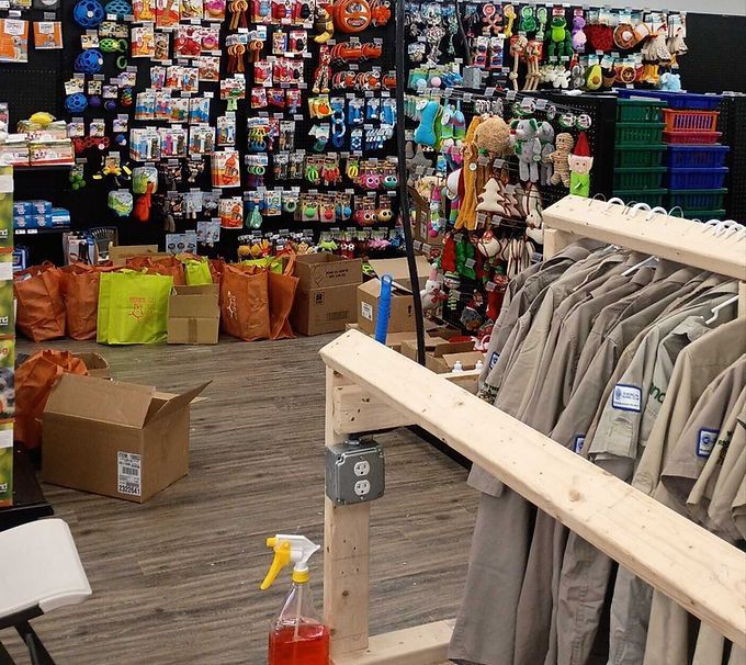Shop aisle with hanging clothes, colorful merchandise displays, and a cardboard box on a wooden floor.