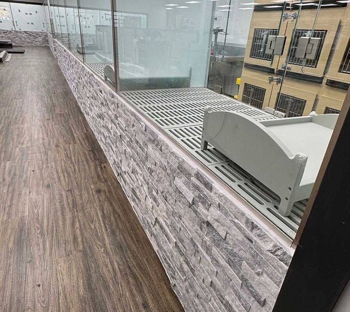 Glass-railed walkway beside a stone-textured wall and wood floor in a modern interior.
