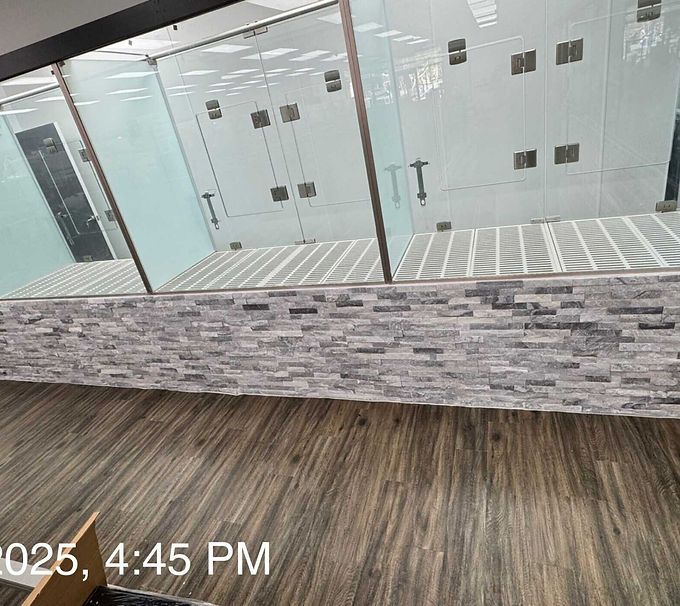 Indoor glass corridor with stone half-wall and wood-look flooring; timestamp visible at bottom left.