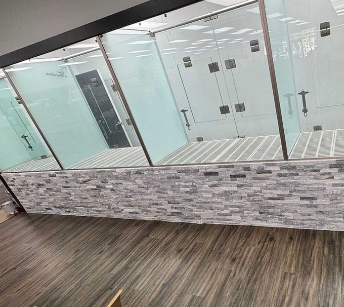 Modern bathroom with glass shower stalls, gray tile, and wood-pattern flooring