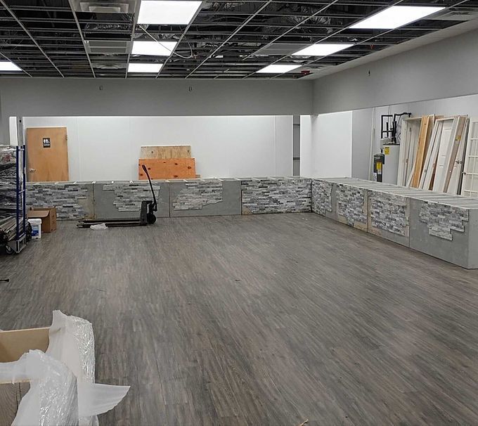 Empty tiled showroom interior with gray flooring, stacked materials, and ceiling lights