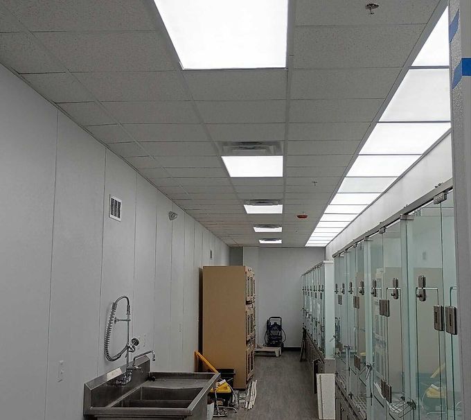 Bright hallway with ceiling lights, sink on the left, and glass-walled rooms on the right.