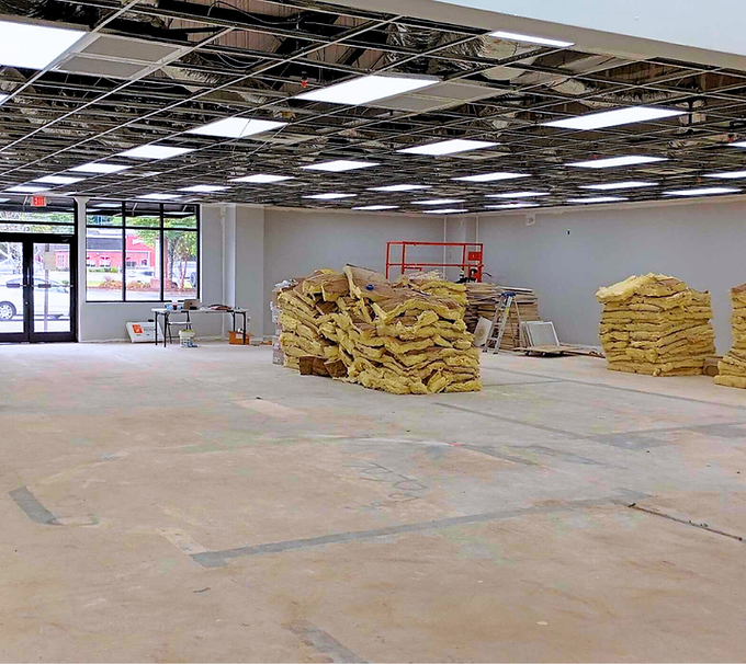 Empty storefront interior under renovation with exposed ceiling, stacked drywall, and glass entrance doors