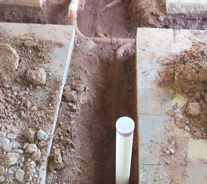 A white PVC pipe protrudes from a dirt trench between two concrete slabs.