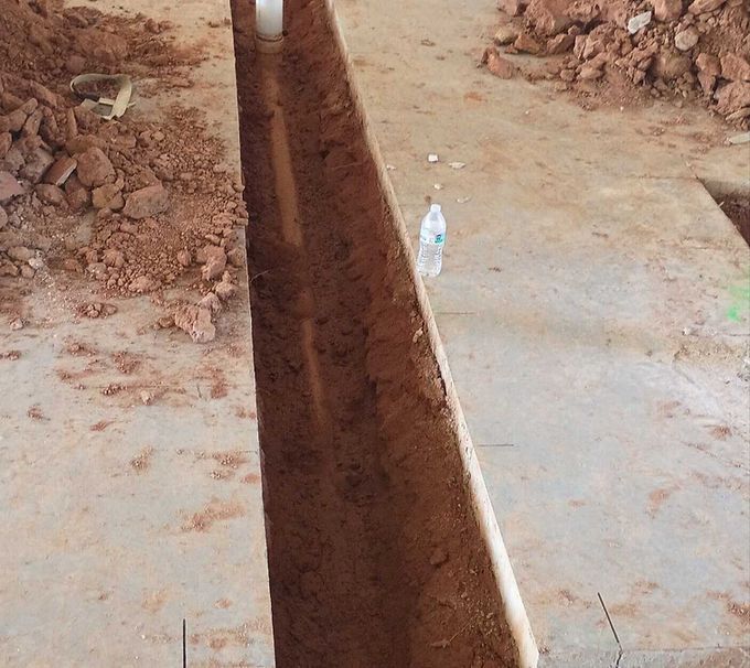 A deep trench cut through a dirt surface beside a concrete path, with a water bottle for scale.