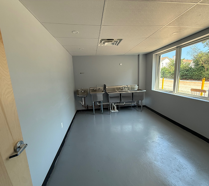 Small empty room with a sink counter, chair, and large window letting in daylight