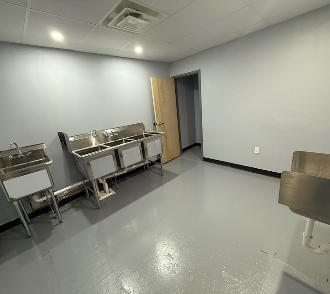 Empty break room with stainless steel sinks, gray floor, and an open door.