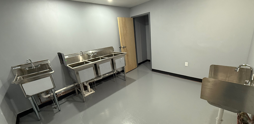 Empty break room with stainless steel sinks, a table, gray walls, and an open door