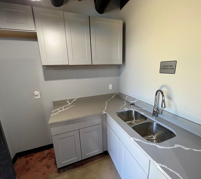 Small modern kitchenette with white cabinets, gray counters, and a stainless steel double sink.