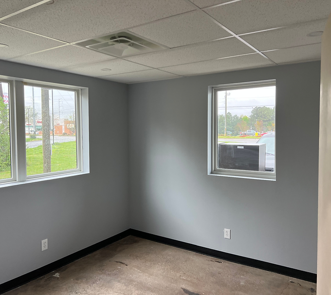 Empty gray room with two windows, white ceiling tiles, and unfinished floor