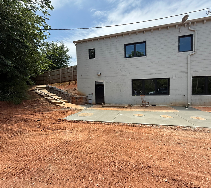 White two-story house with a concrete patio and dirt yard under construction