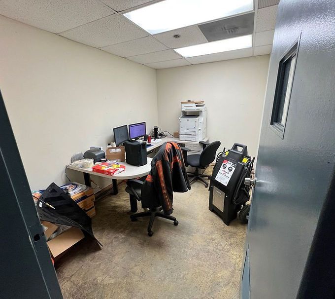 Small office with desks, computer monitors, chairs, and boxes in a cramped workspace