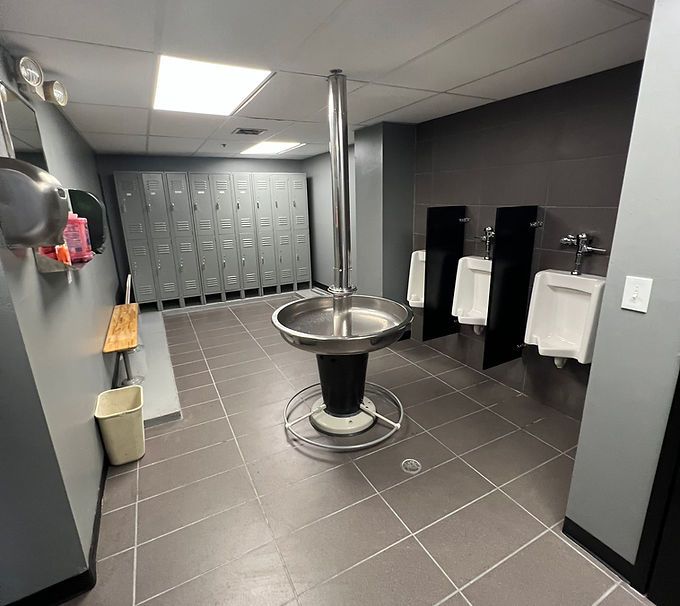Modern restroom with gray tile, central sink, lockers, and white urinals along the wall