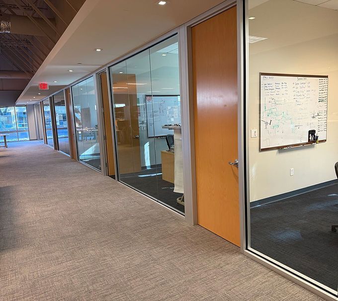 Office hallway with glass-walled rooms, wooden doors, and a whiteboard on the wall