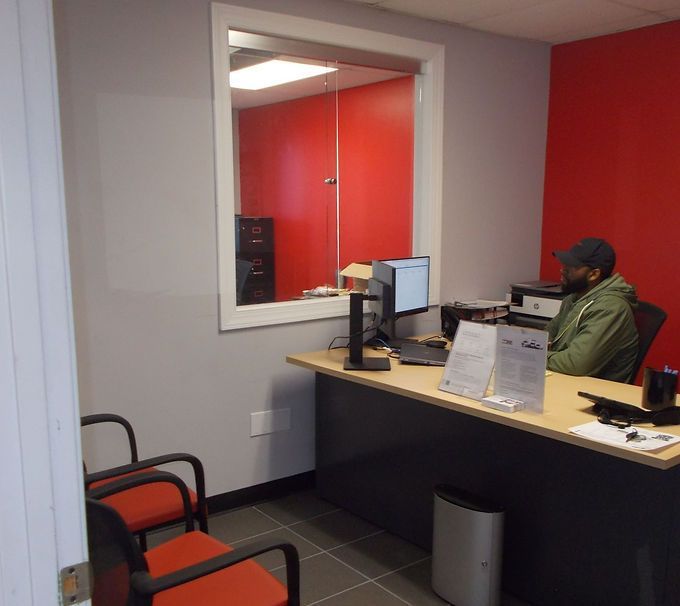 Office reception area with a seated person behind a desk, red walls, and two chairs in the foreground
