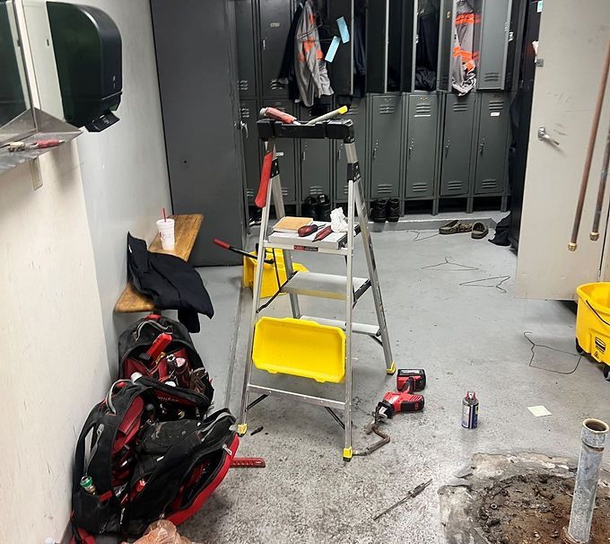 Cluttered utility room with a ladder, tools, lockers, and paint supplies on a dirty floor.