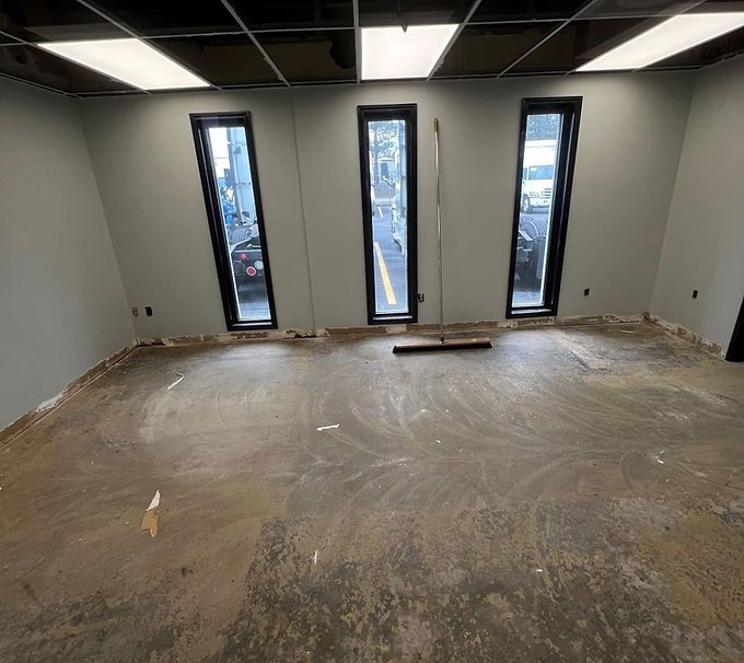 Empty modern room with unfinished concrete floor and three tall narrow windows.