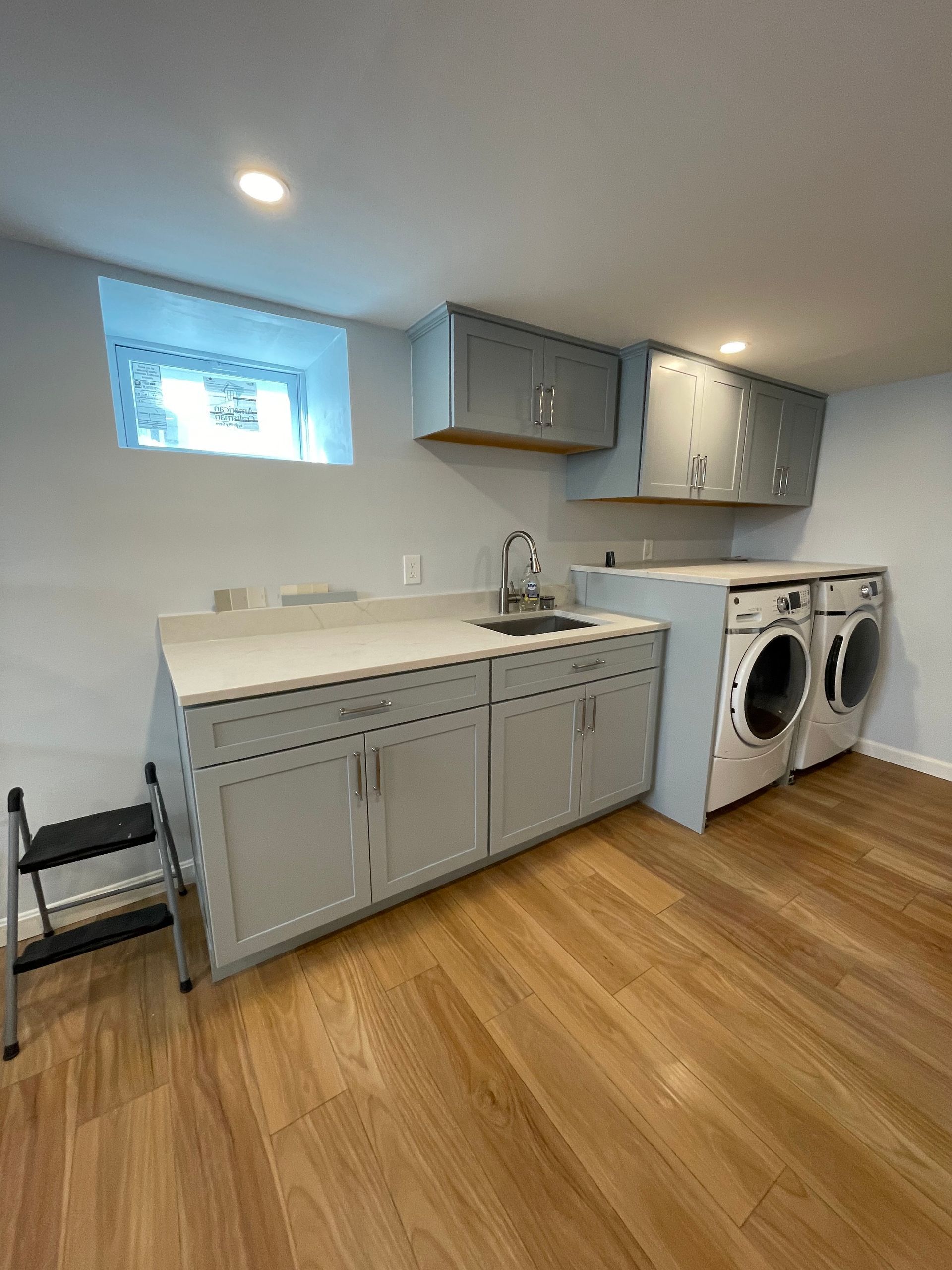 Small laundry room with gray cabinets, sink, countertop, washer and dryer, and wood flooring.