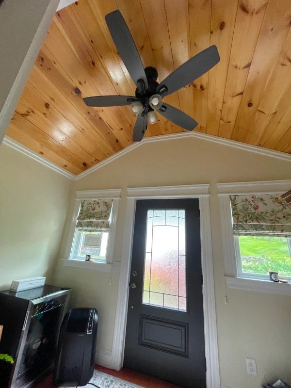 Small entryway with wood plank vaulted ceiling, ceiling fan, front door, and two windows.