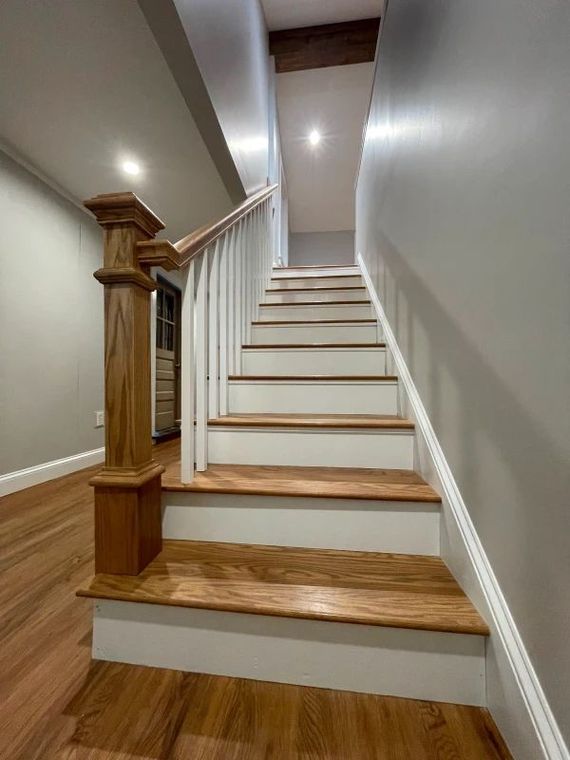 Indoor staircase with wood steps, white walls, and a wooden banister viewed from the bottom.