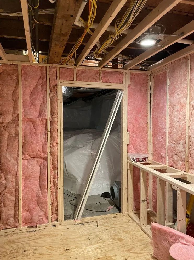 Unfinished room with exposed framing, pink insulation, and a doorway to a dark adjacent space