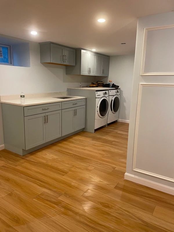 Basement laundry room with gray cabinets, washer and dryer, recessed lights, and wood floors