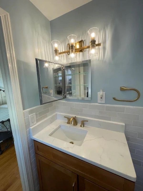 Bathroom vanity with white countertop, brass faucet, wall mirror, and light blue walls.