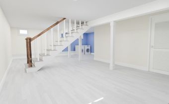 Bright white living room with wooden staircase, open doorway, and minimal modern interior.