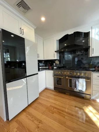 Bright modern kitchen with white cabinets, black appliances, stainless stove, and wood floors
