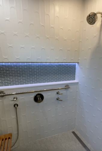 Minimalist bathroom shower with white textured tiles, blue accent strip, handheld shower, and circular showerhead.