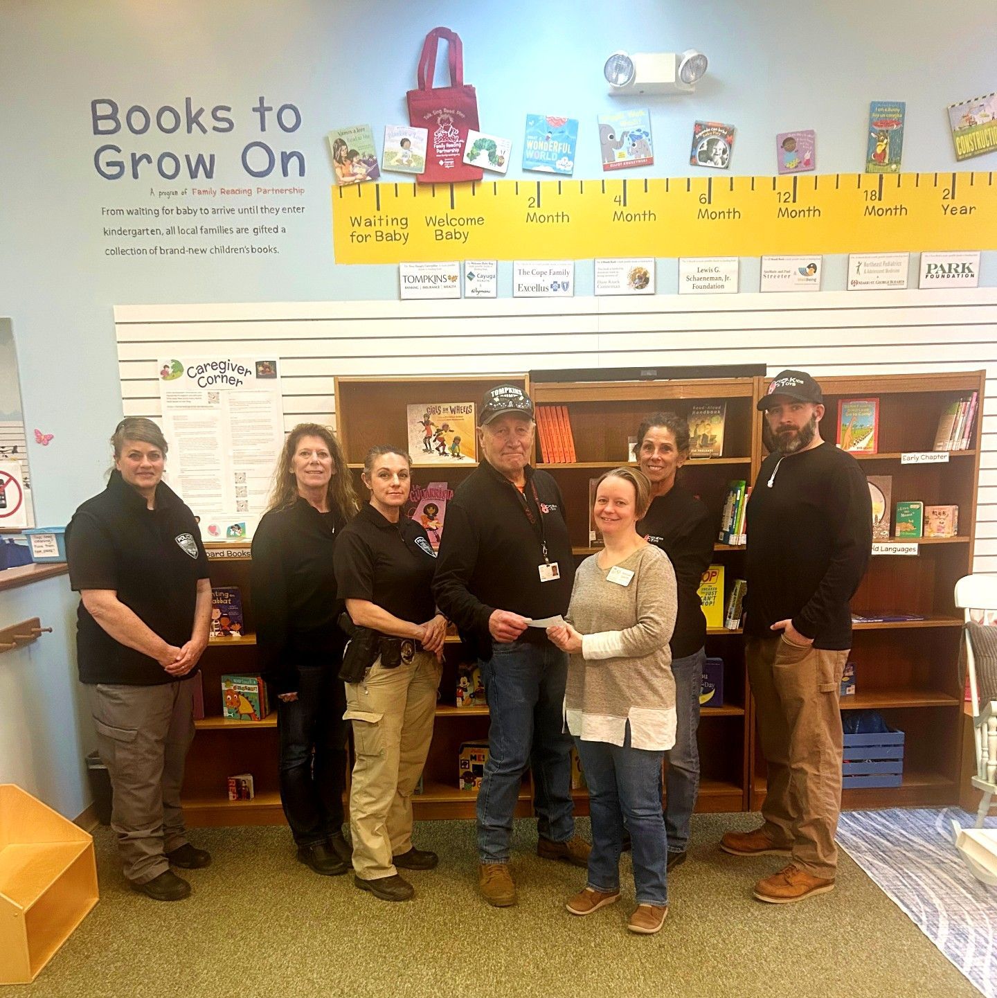 Group presents check in bookstore. People smile, posing in front of bookshelf. 