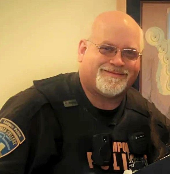 A bald man with a beard and glasses is wearing a police uniform.