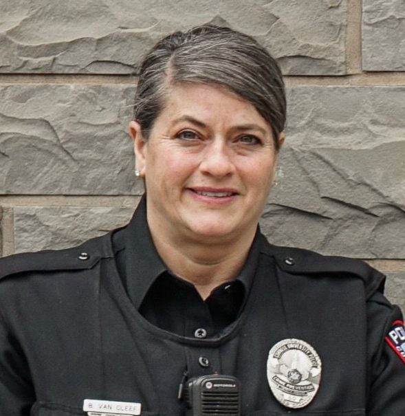 A woman in a police uniform is smiling and holding a walkie talkie