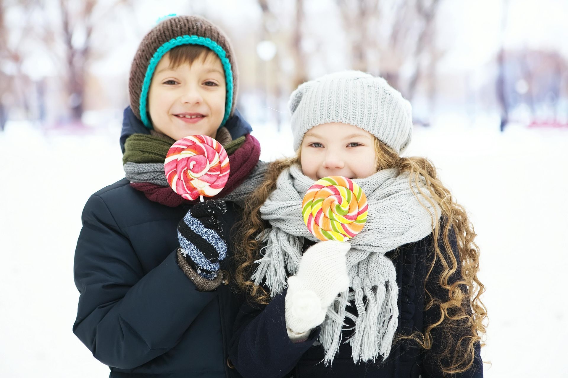 A boy and a girl are eating lollipops in the snow.