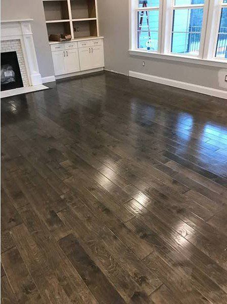 Empty living room with dark hardwood floors, white walls, fireplace, built-in shelves, and large windows.