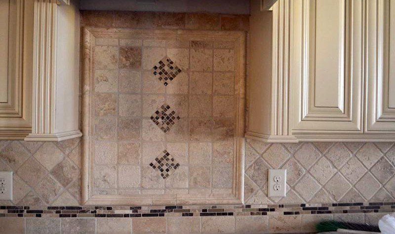 Kitchen backsplash with beige tile, decorative diamond accents, and cream cabinets above a countertop