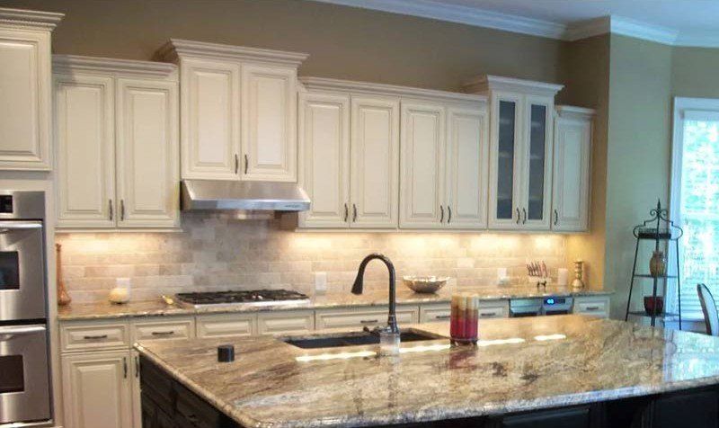 Modern kitchen with white cabinets, granite island, stainless hood, and sink under pendant lighting