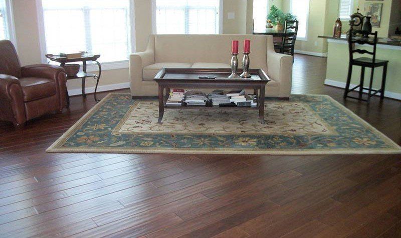 Living room with hardwood floors, large area rug, coffee table, sofa, and armchairs near bright windows