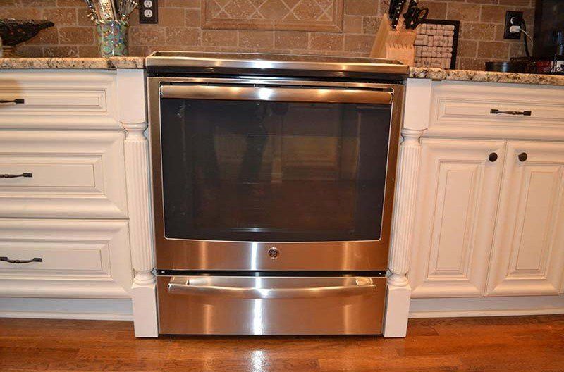Stainless steel oven centered between white kitchen cabinets on a wood floor.