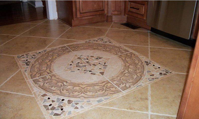 Decorative mosaic medallion in a beige tiled kitchen floor near wooden cabinets
